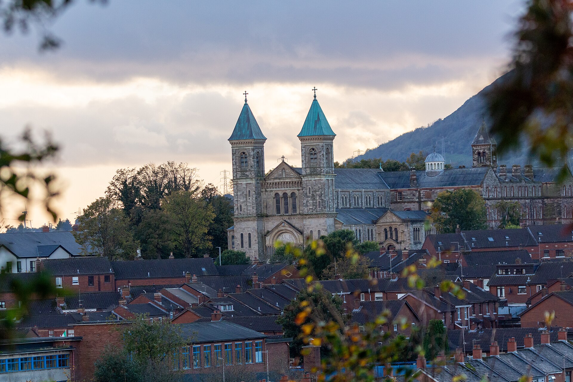 Red-brick rooftops of Ardoyne in north Belfast, with the twin green spires of Holy Cross Church and the hills behind